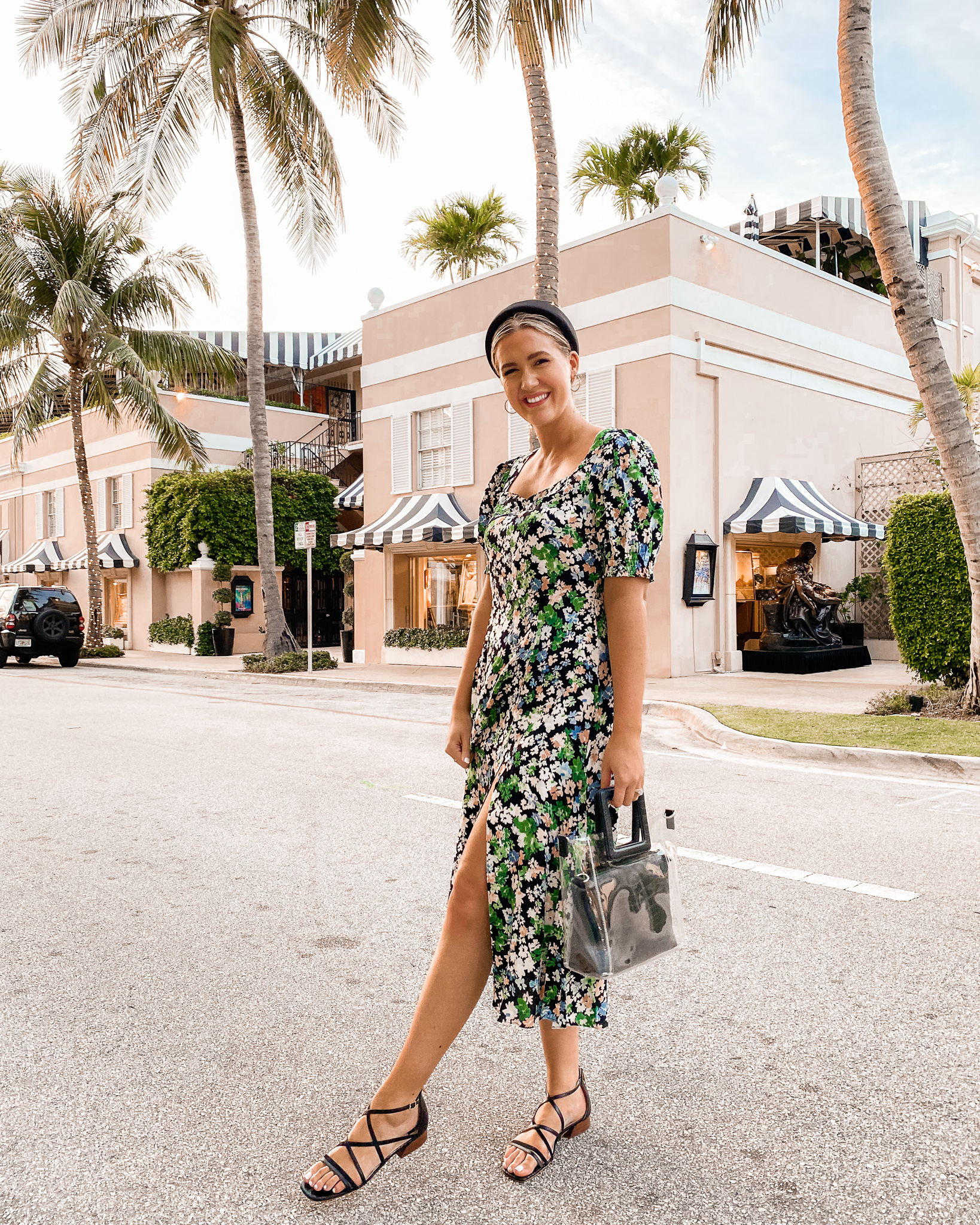 Anna wearing a dress standing in the street of a tropical place with palm trees in the background.