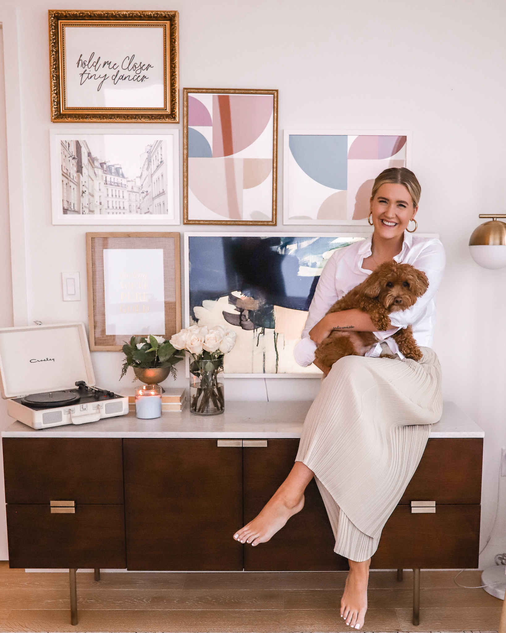 Anna's apartment with her standing in front of her gallery wall with her dog, Banks.