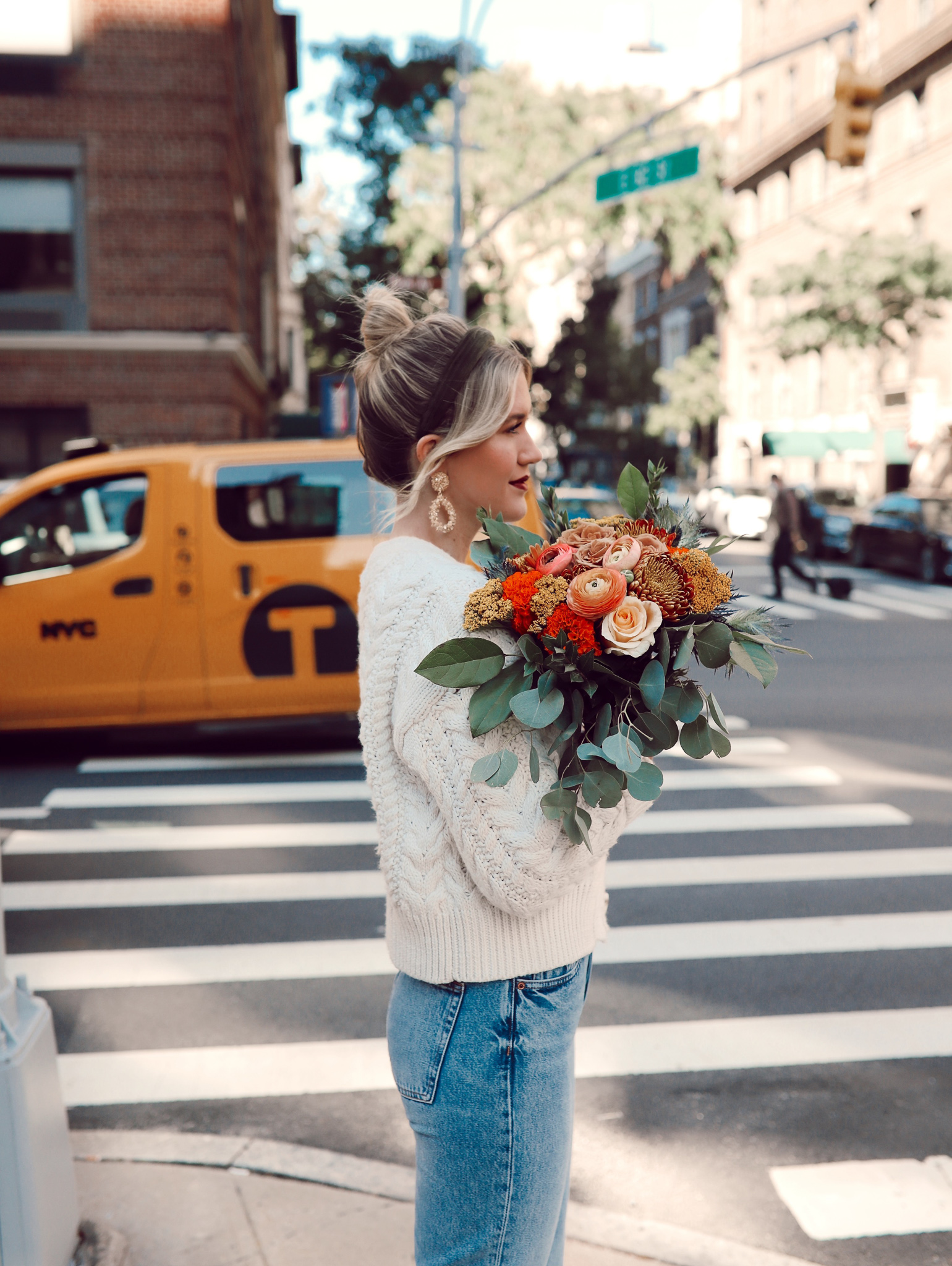 Anna in the street of New York City with a yellow taxi in the back with flowers in her hand.