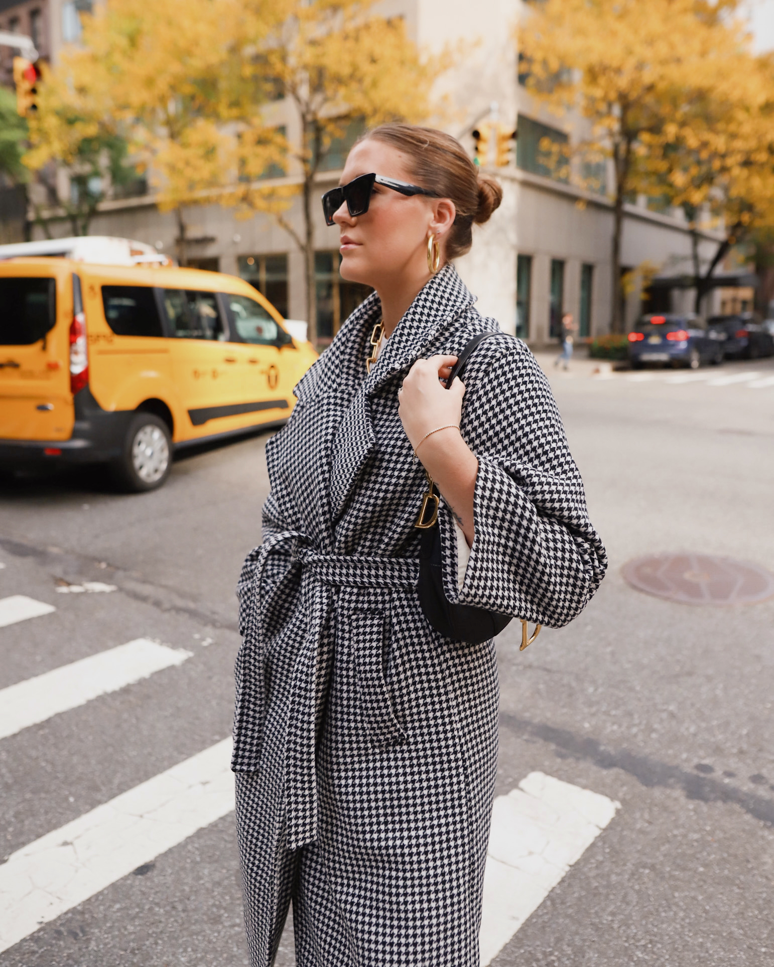 Anna standing in New York City street with gray coat and sunglasses on with yellow taxi in background.