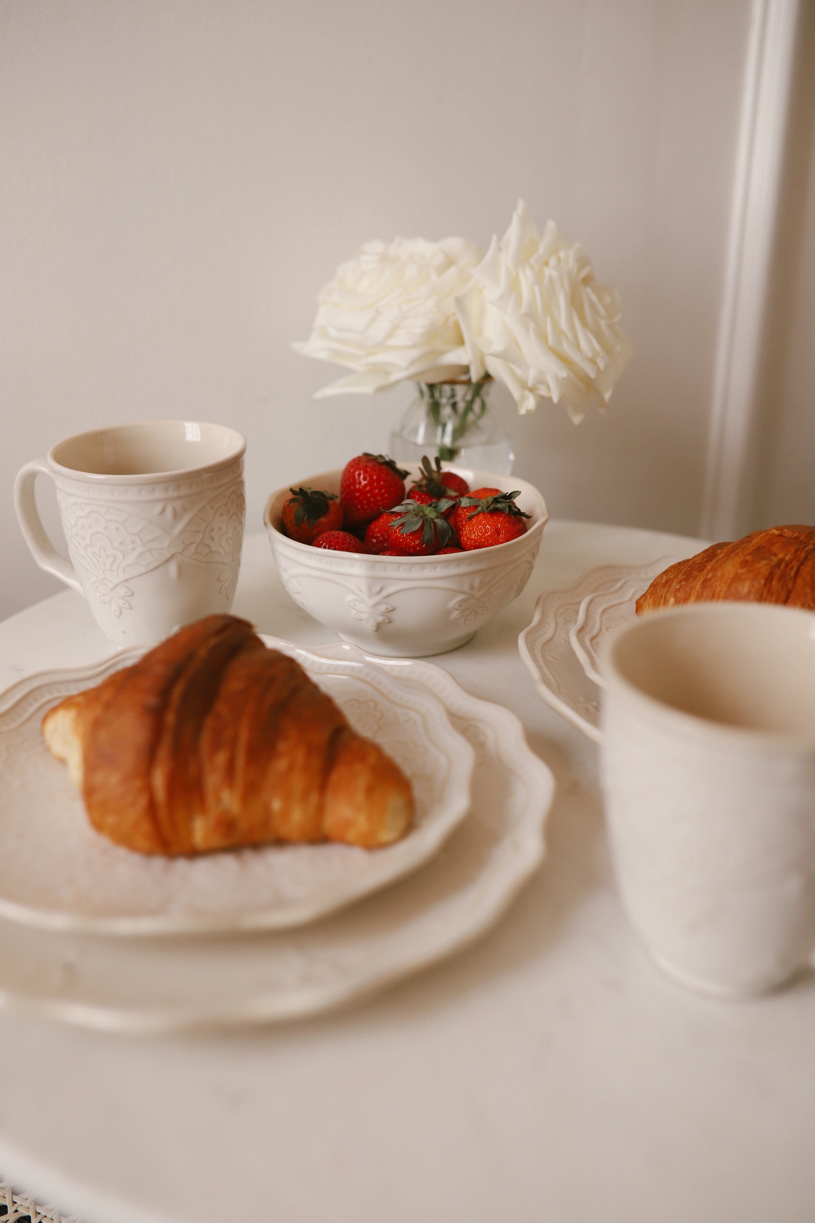 Croissant, coffee mugs, flowers, and fruit.