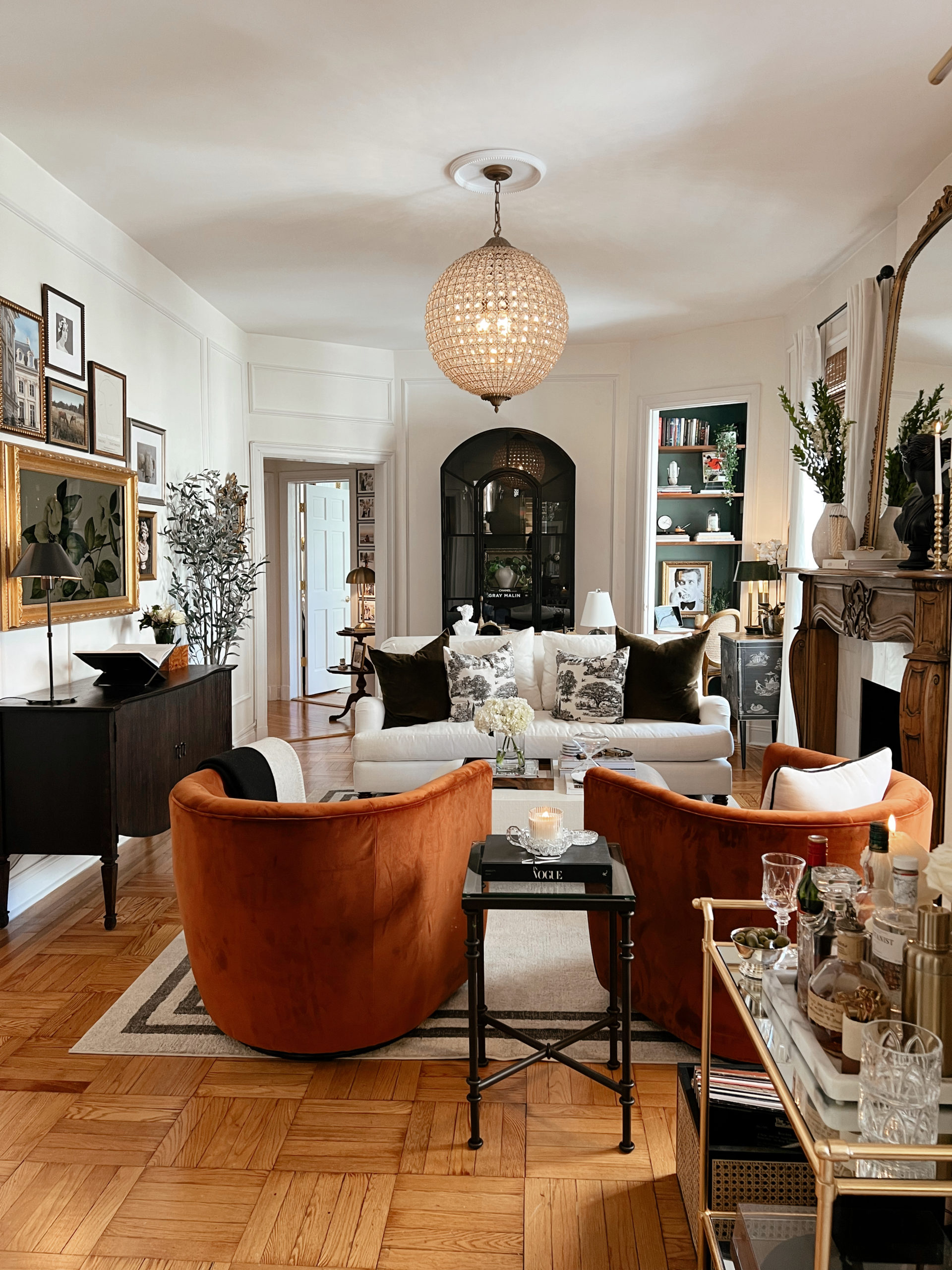 Anna's Upper East Side living room with two big orange chairs, a white couch, and a beautiful chandelier.