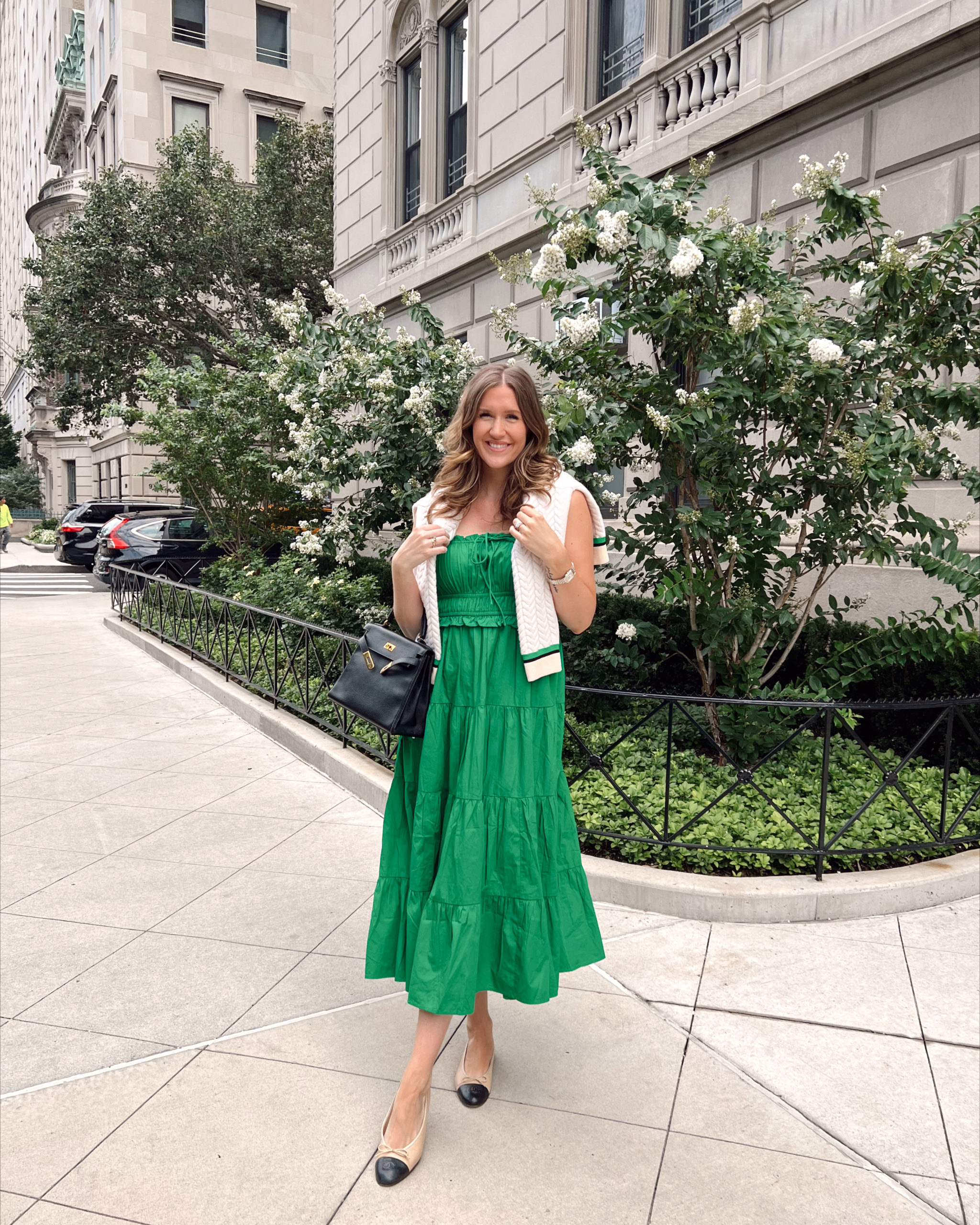 Anna wearing a green dress and an ivory cardigan thrown over her neck on the sidewalks of New York City.