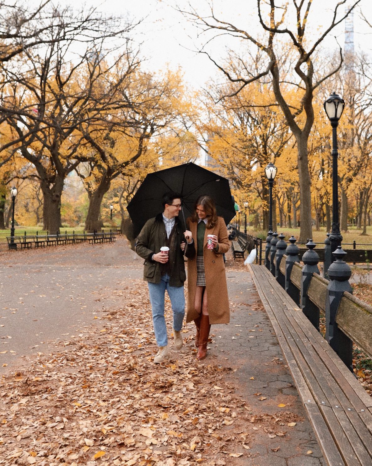 Anna and Nathan walking in Central Park with an umbrella during the fall season.