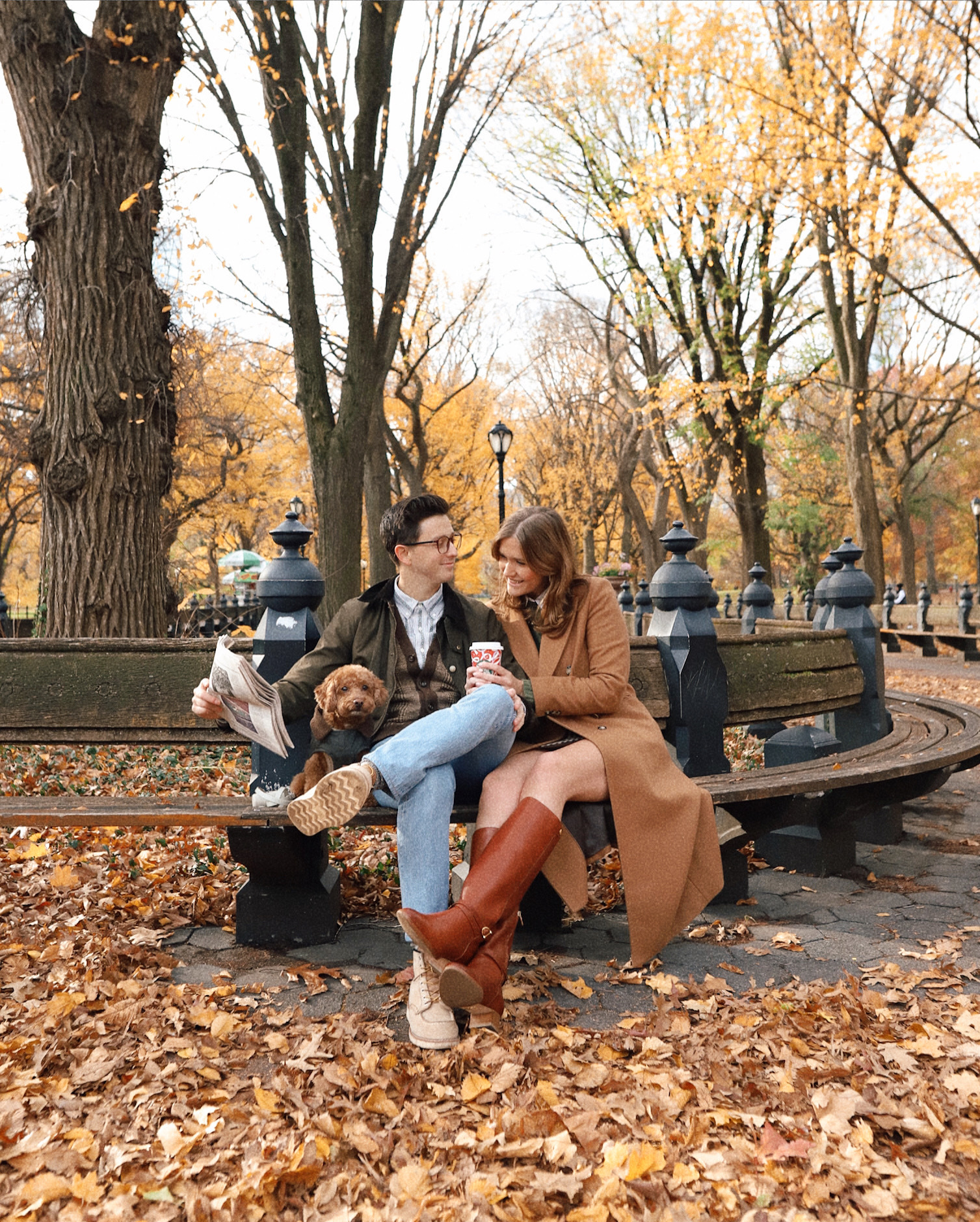 Anna and Nathan sitting in Central Park during the fall time with leaves all around them.