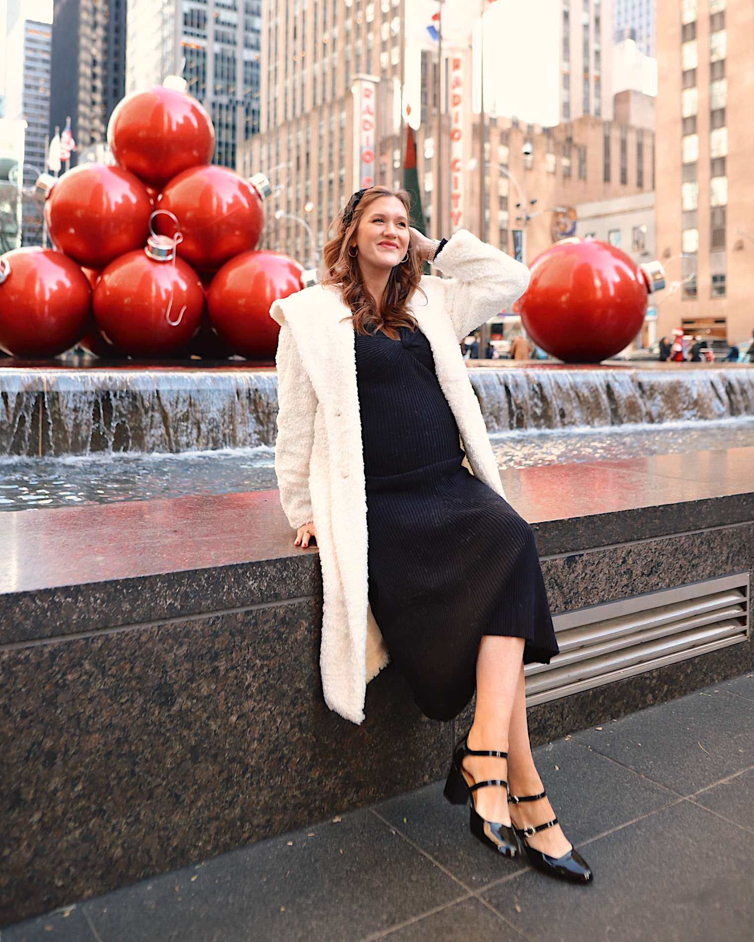 Anna in front of large red ornaments on 5th Avenue in New York City.