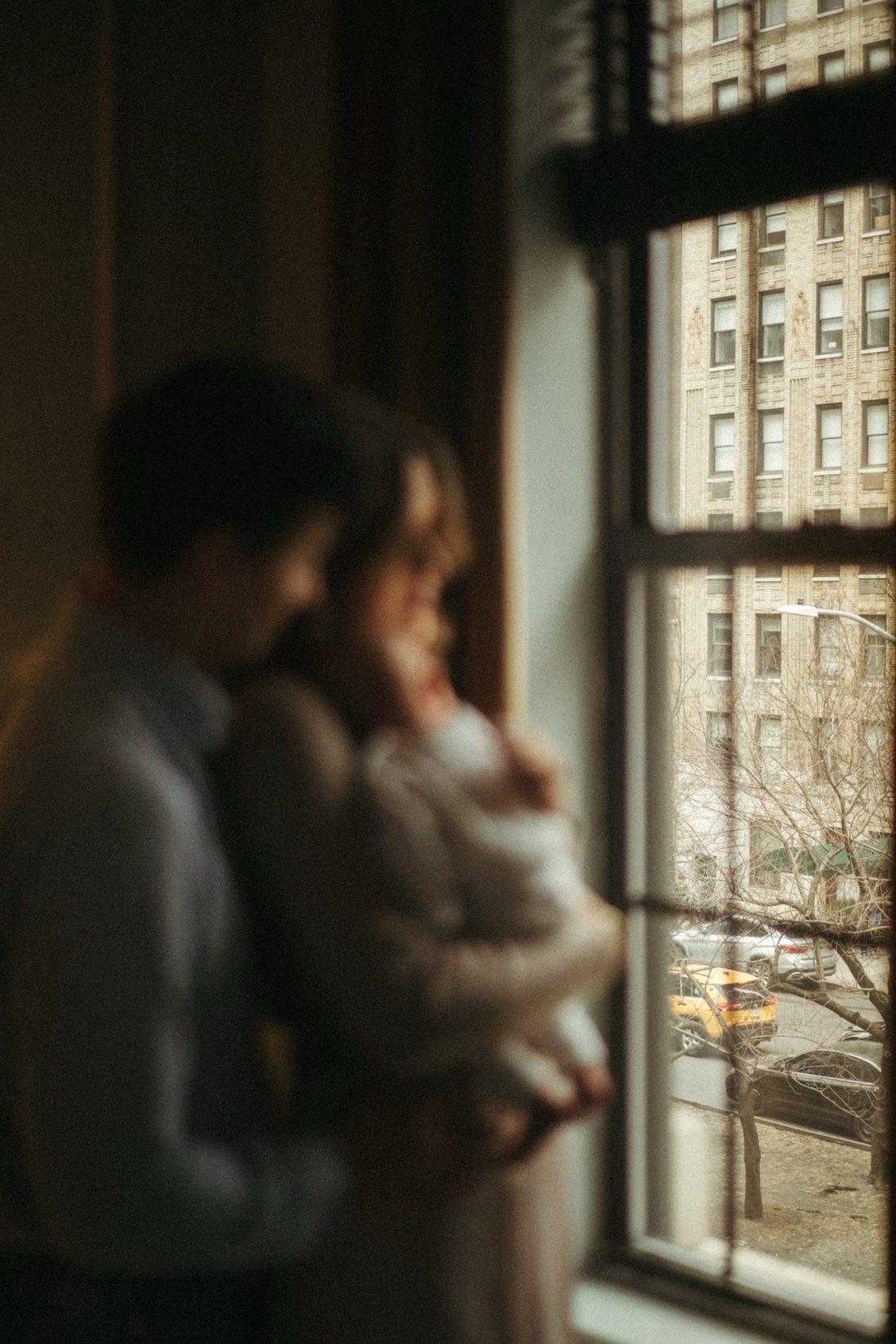Anna and Nathan looking out a window with their newborn.