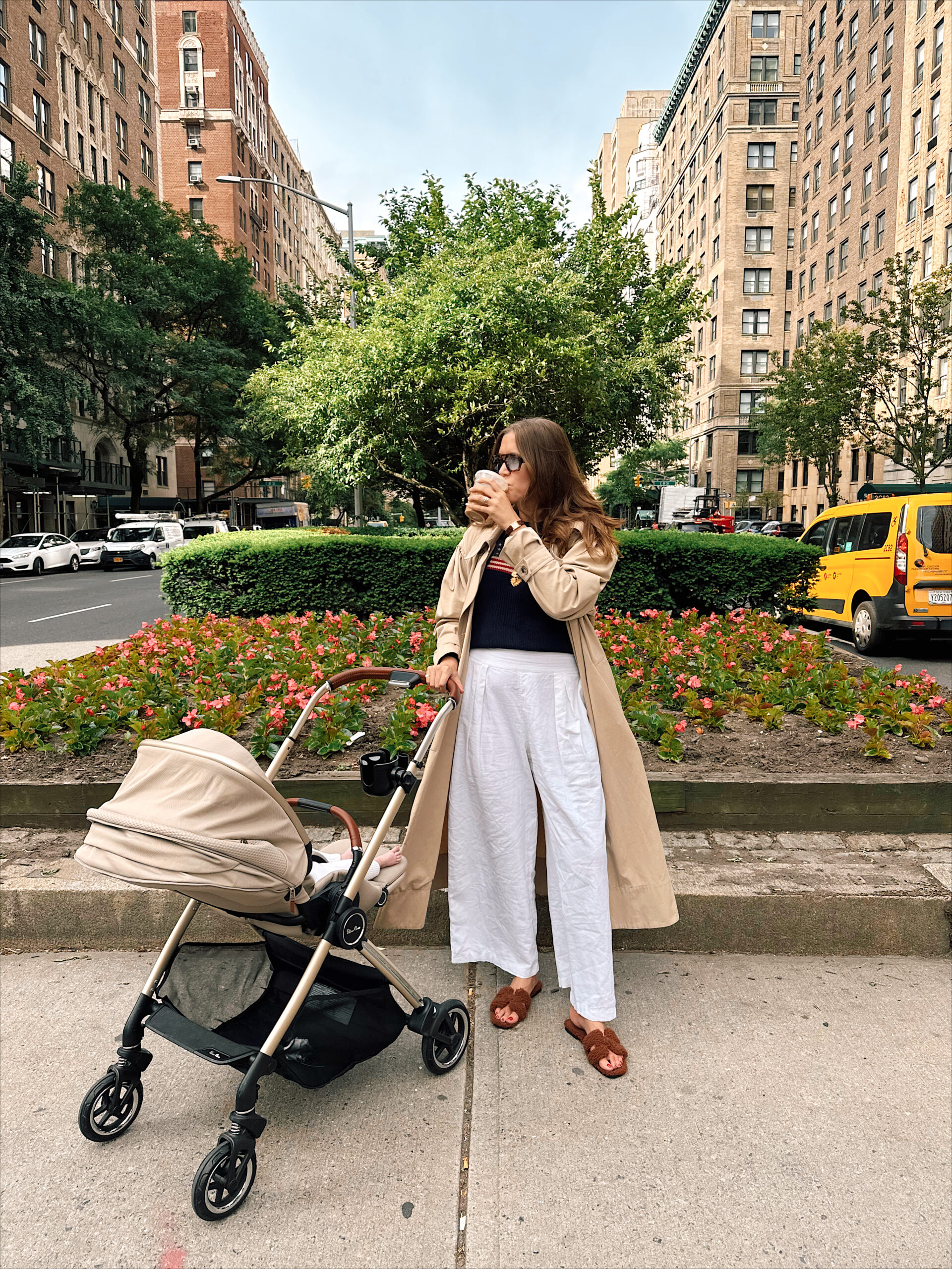 Anna Page on Park Avenue on a spring day with her baby in a stroller and coffee in hand as taxis drive past in the background.