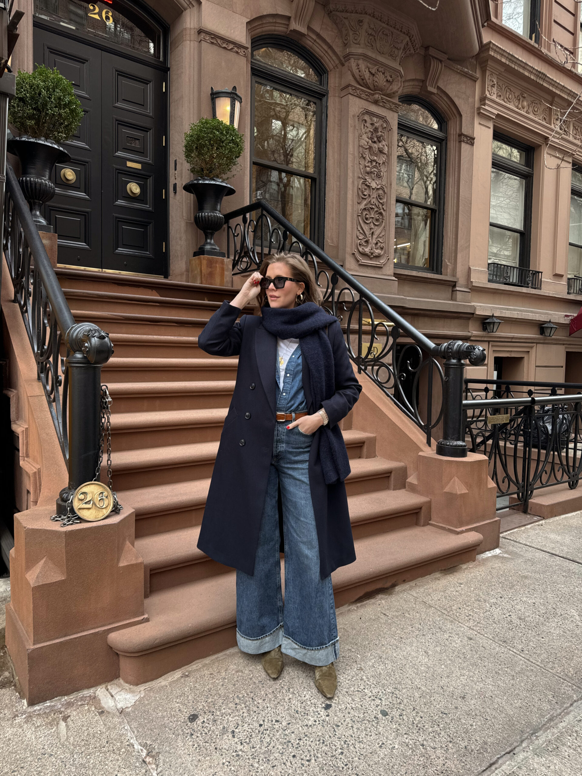 Anna wearing a long dark colored peacoat and jeans in front of New York City stoop.